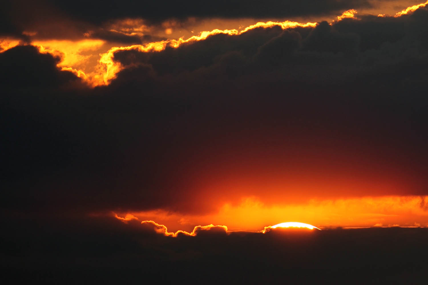 Foto der untergehenden Sonne kurz vor dem Abtauchen hinter dunklen Wolken